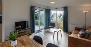 A modern living room with a wooden dining table, a sofa, a TV, and a large sliding glass door leading to a garden. - Cozy Chalet at Holiday Park Fort den Haak (Vrouwenpolder)