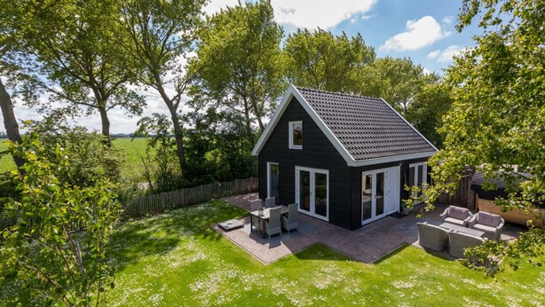 A small house with a dark exterior, a sloped roof, and a patio area with outdoor furniture. - Holiday Home in Vrouwenpolder With Garden (Vrouwenpolder)