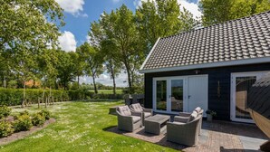 A modern house with a tiled roof, a patio with wicker furniture, and a well-maintained garden. - Holiday Home in Vrouwenpolder With Garden (Vrouwenpolder)