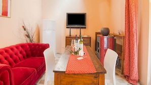 Una sala de estar acogedora con un sofá rojo, una mesa de comedor de madera con mantel rojo, un televisor en la pared y una chimenea.