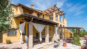 Un edificio amarillo con un patio cubierto, mesas al aire libre y una pérgola.