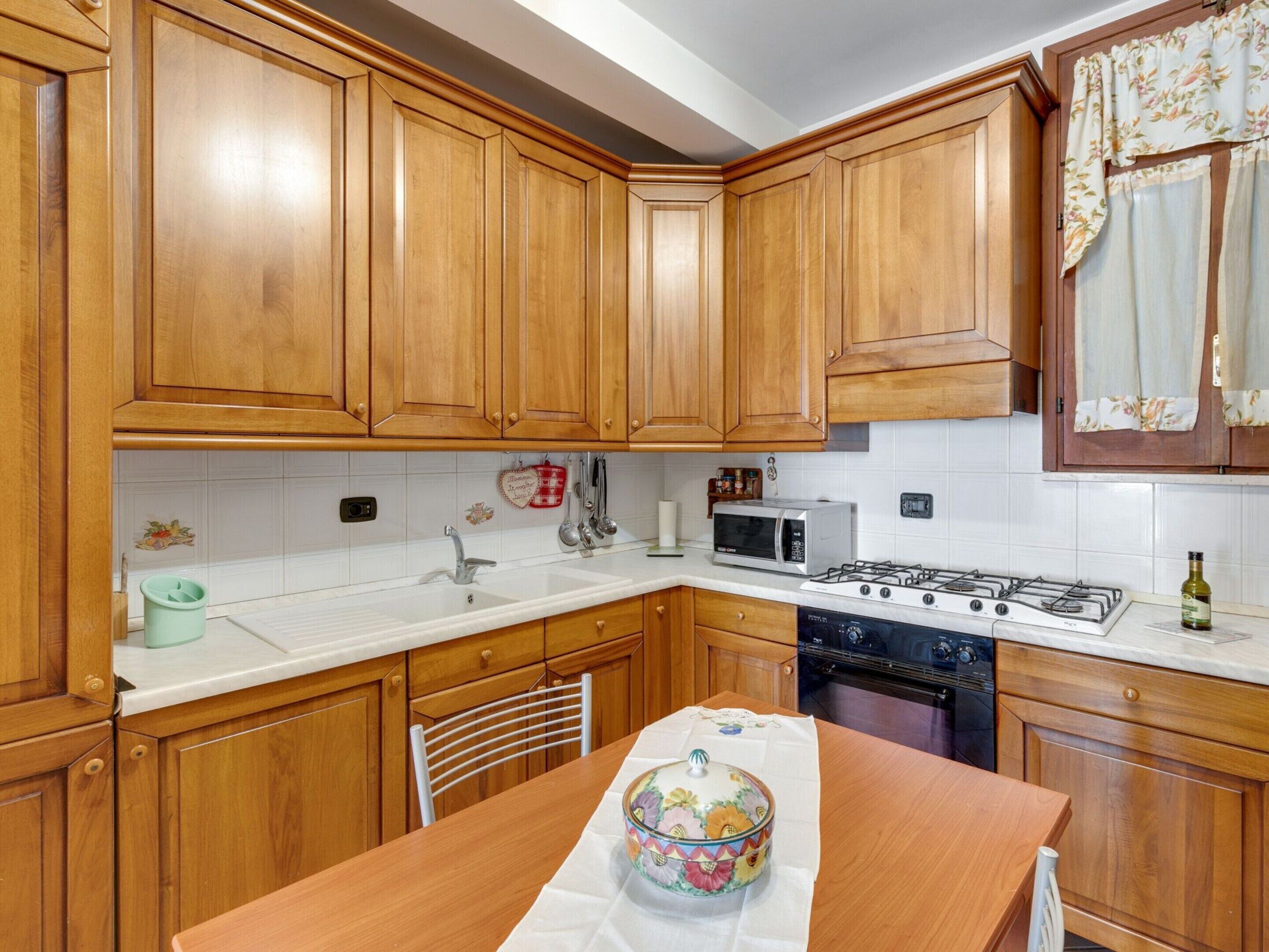 A kitchen with wooden cabinets, a microwave, stove, sink, and a table with a decorative bowl.