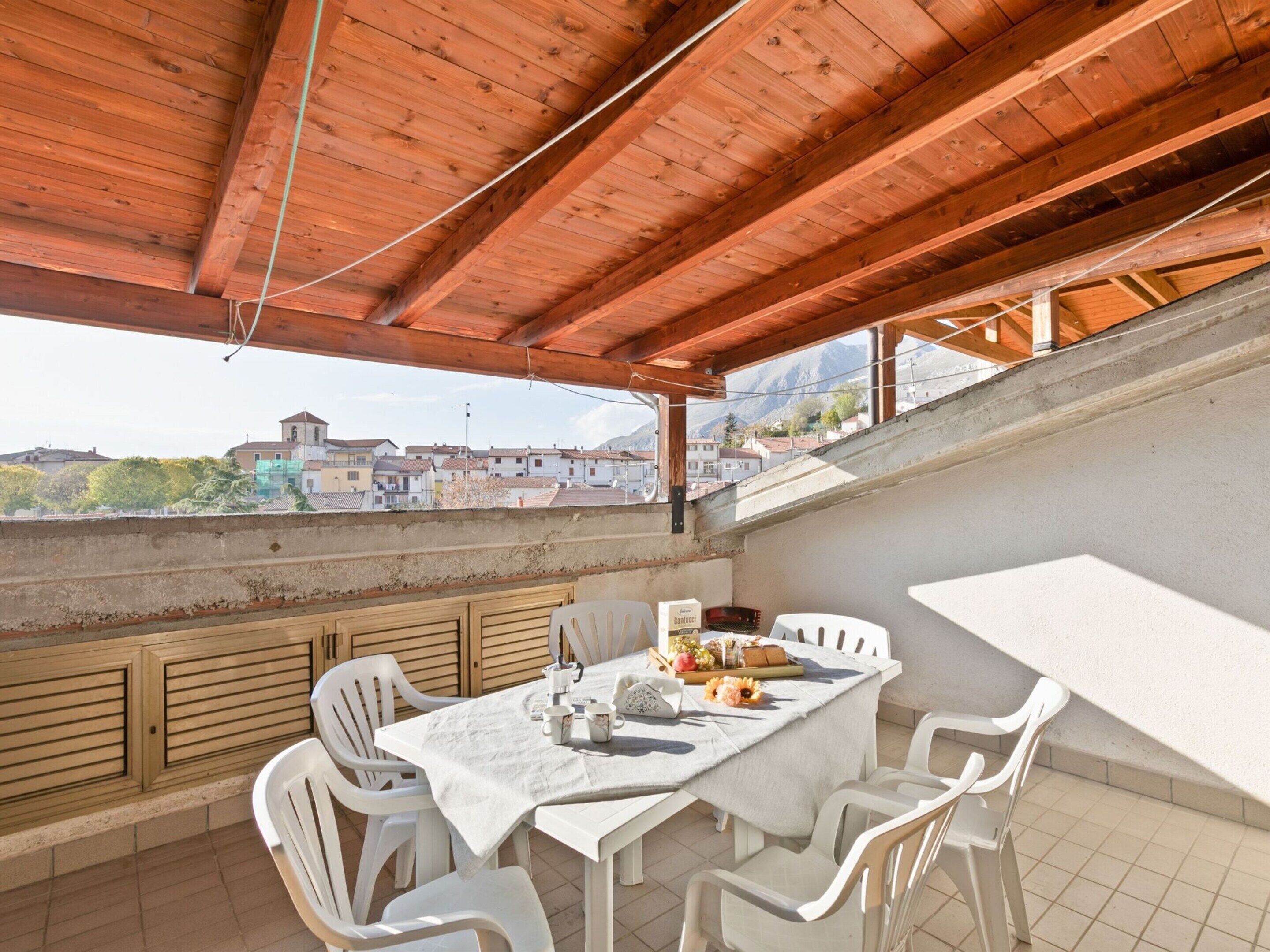 A covered outdoor dining area with a table and chairs, overlooking a town and mountains.