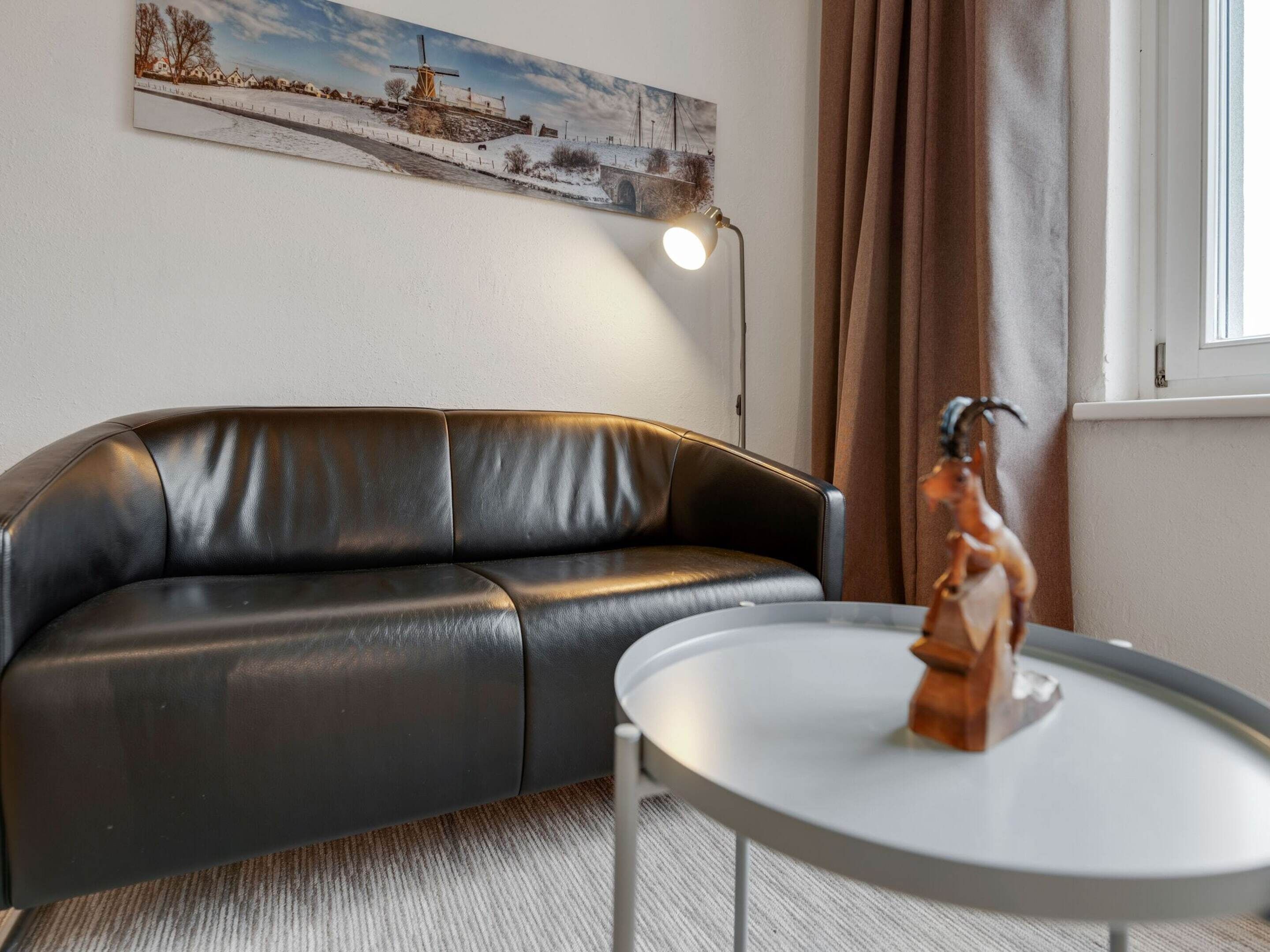 Una sala de estar moderna con un sofá de cuero, una mesita redonda, una escultura decorativa, una lámpara de pie y un cuadro en la pared.