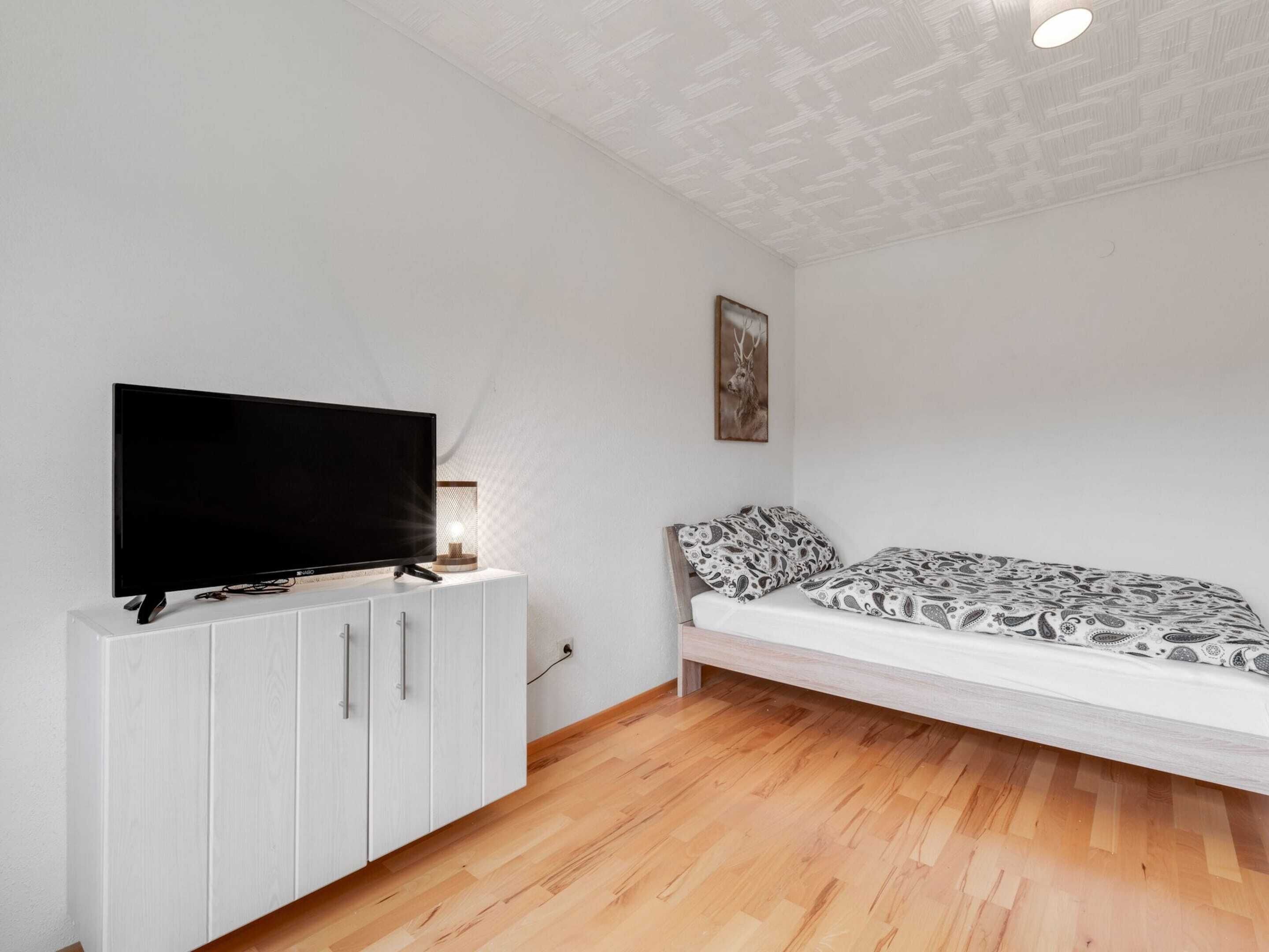 A bedroom with a bed, a TV on a cabinet, and a ceiling light.
