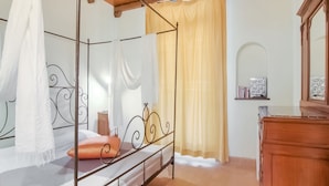 A four-poster bed with a canopy, a wooden dresser, and a small bedside table with a lamp. - Apartment in Ascoli Near Mountains (Ripatransone)