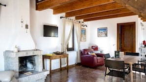 A spacious living room with a stone fireplace, wooden ceiling beams, a red leather sofa, and a dining area with a table and chairs. - Serene Apartment in Ascoli Piceno with Hot Tub (Ripatransone)