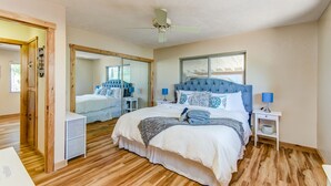 Une chambre avec un grand lit, un ventilateur de plafond, un miroir et une fenêtre avec des stores.