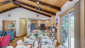 Une salle à manger spacieuse avec une longue table dressée pour six personnes, une cuisine à l’arrière-plan et une grande porte-fenêtre coulissante donnant sur une terrasse extérieure.