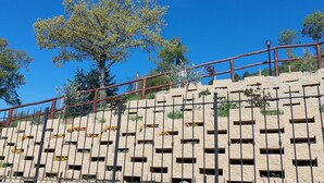 A stone wall with rectangular openings, a metal fence, and a tree.