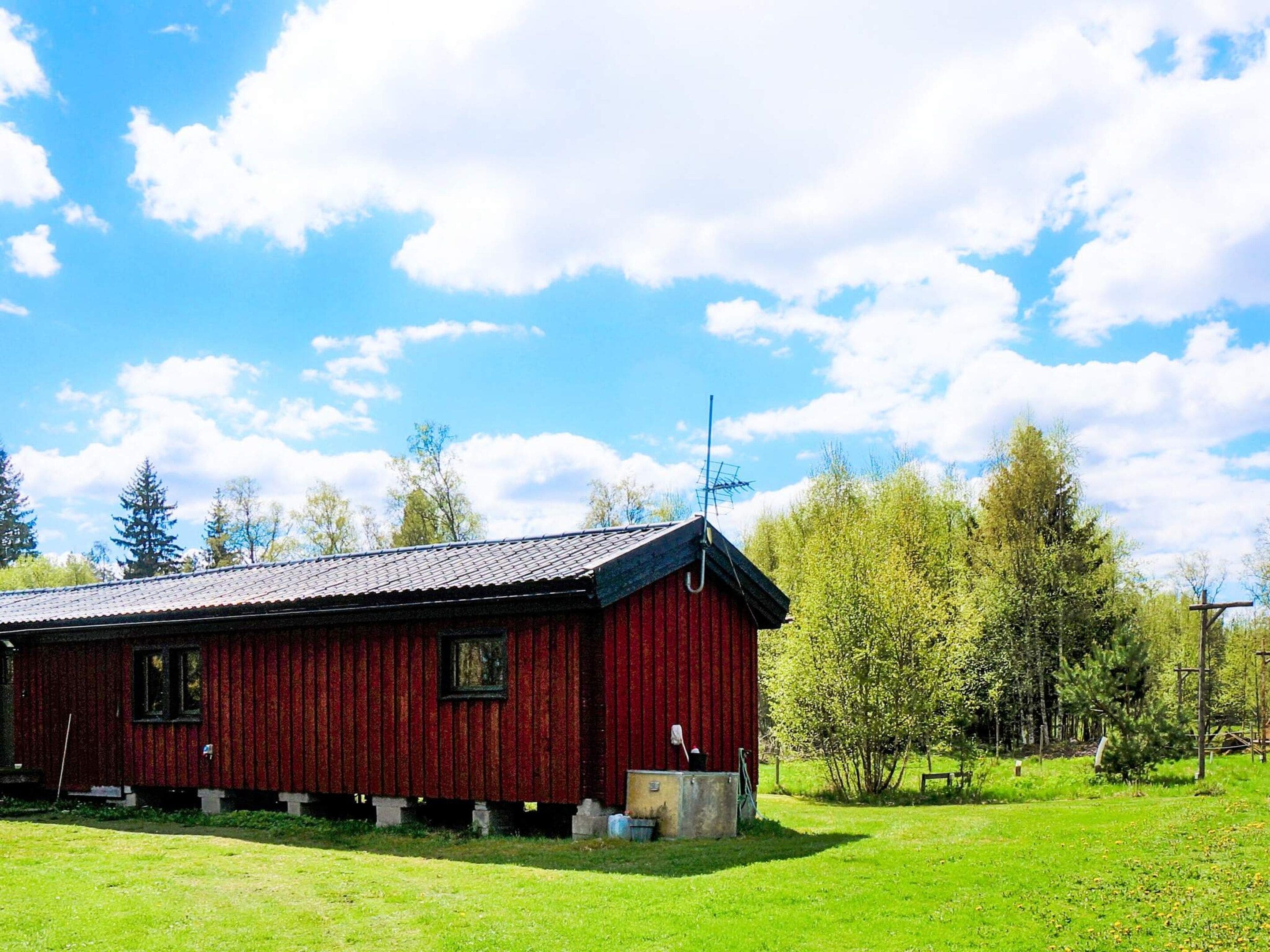 En röd träbyggnad med ett tak av metall, belägen på en gräsyta med träd i bakgrunden.