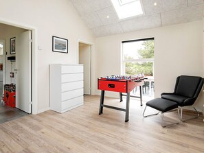 A room with a foosball table, a black chair, a white cabinet, and a window with a view of greenery. - Holiday Home in Thisted (Thisted)