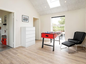 A room with a foosball table, a black chair, a white cabinet, and a window with a view of greenery. - Holiday Home in Thisted (Thisted)