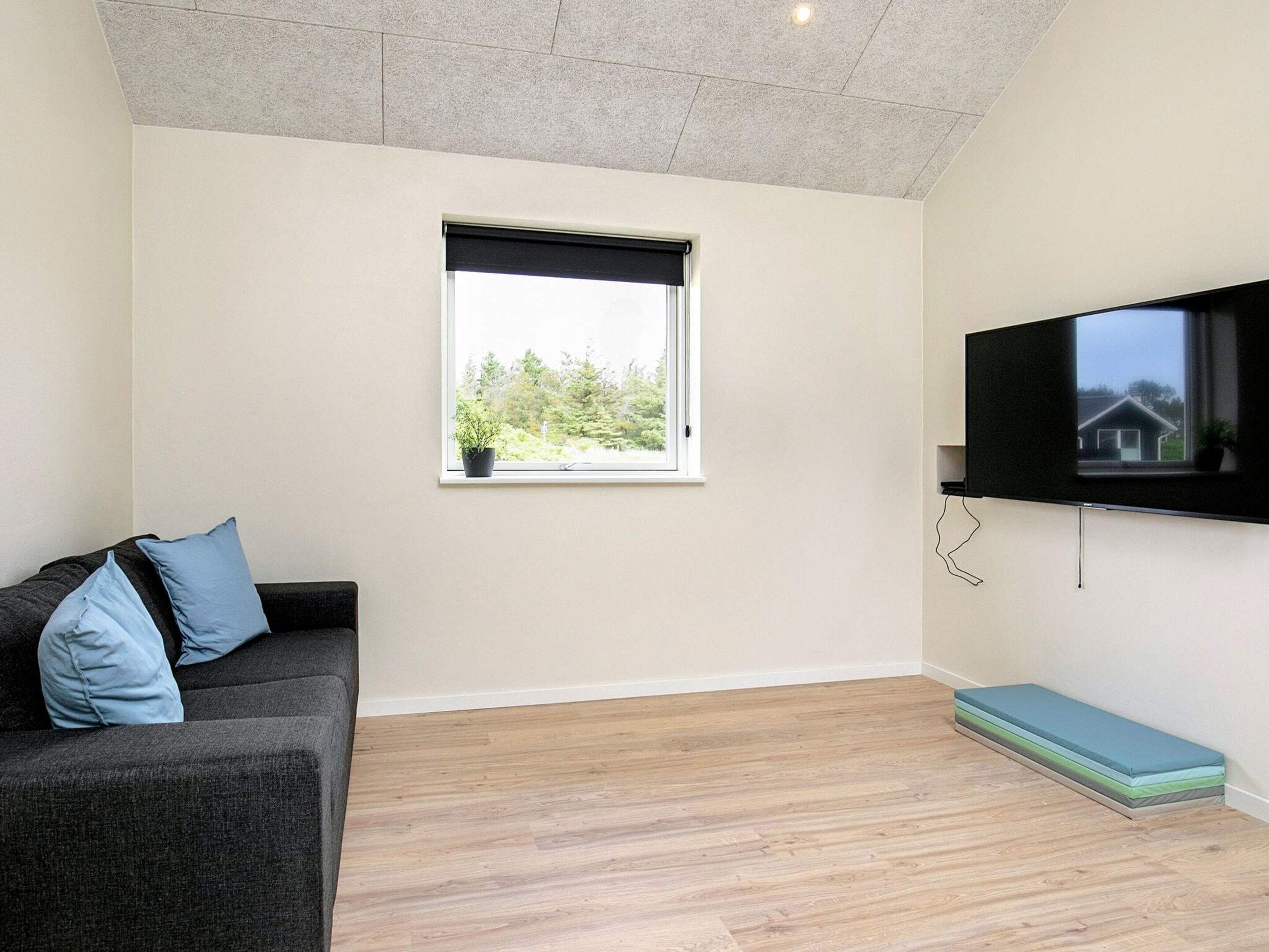 A room with a sofa, a window, a flat-screen TV, and a wooden floor.