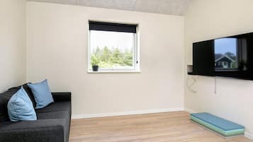 A room with a sofa, a window, a flat-screen TV, and a wooden floor.