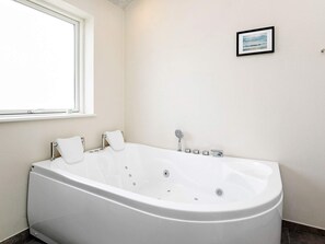 A modern bathroom with a freestanding bathtub, a window, and a framed picture on the wall.