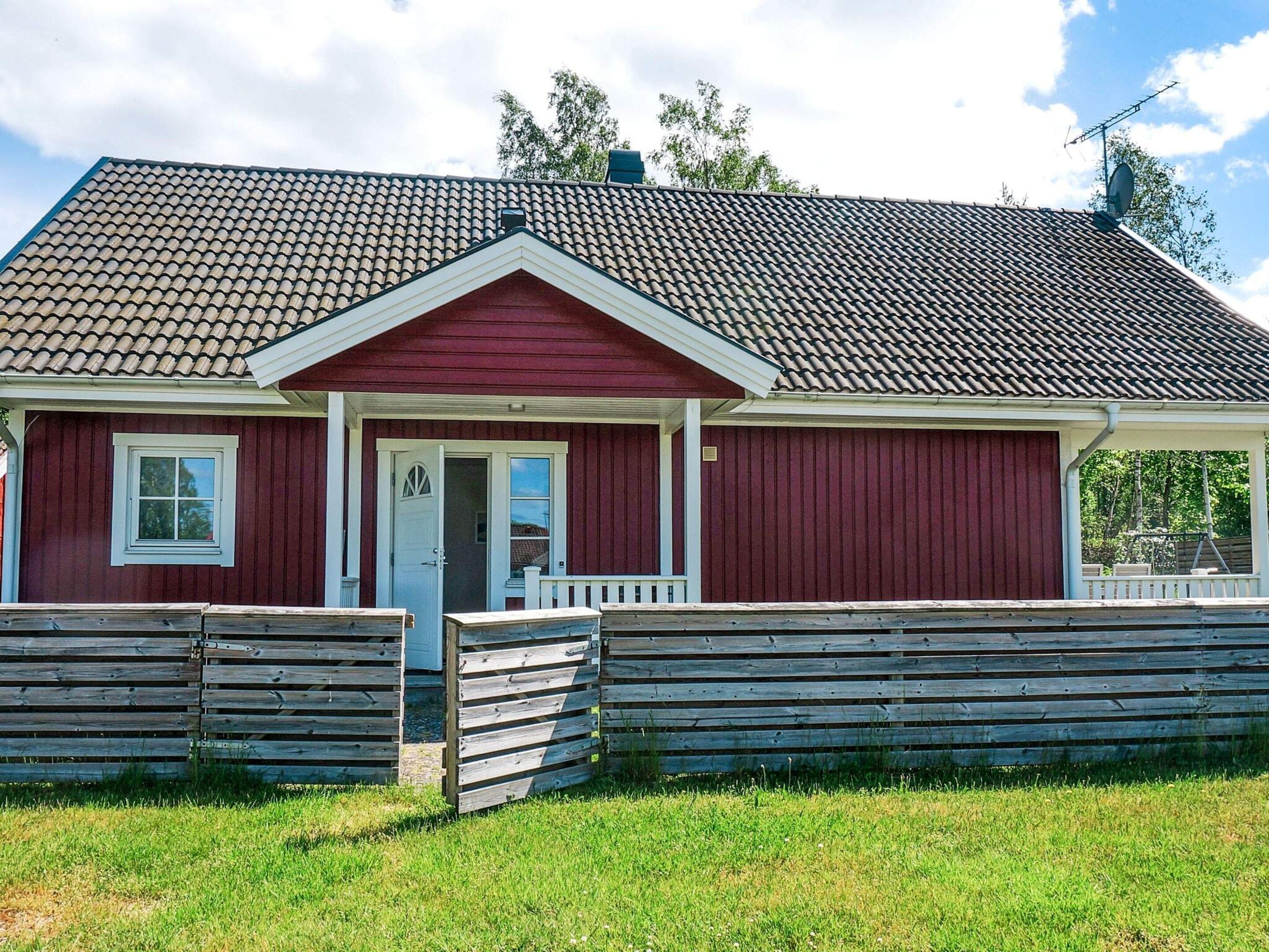 A red wooden house with a white door, a small porch, and a fenced yard.
