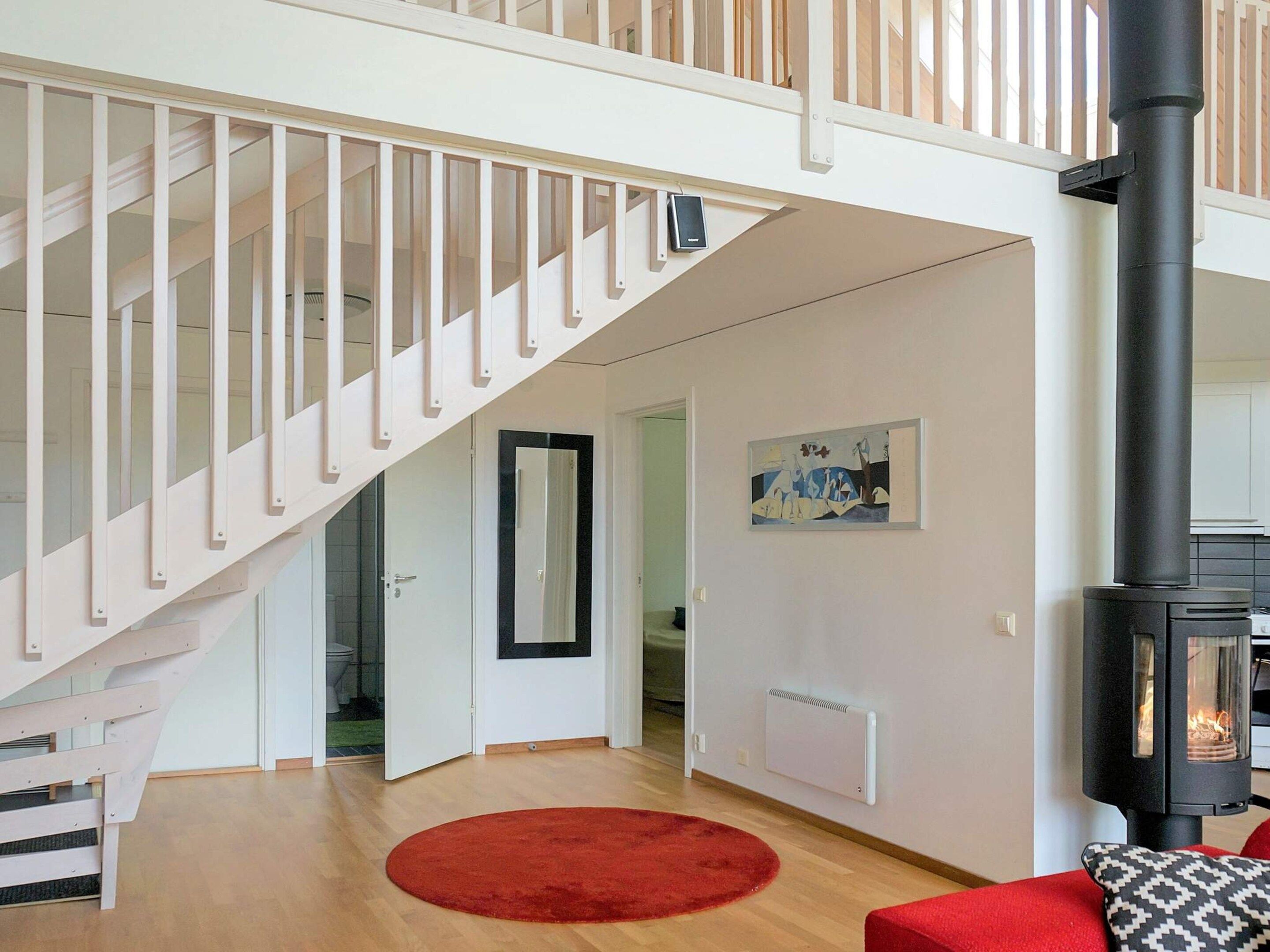 A modern interior with a staircase, a red rug, a black fireplace, and a painting on the wall.