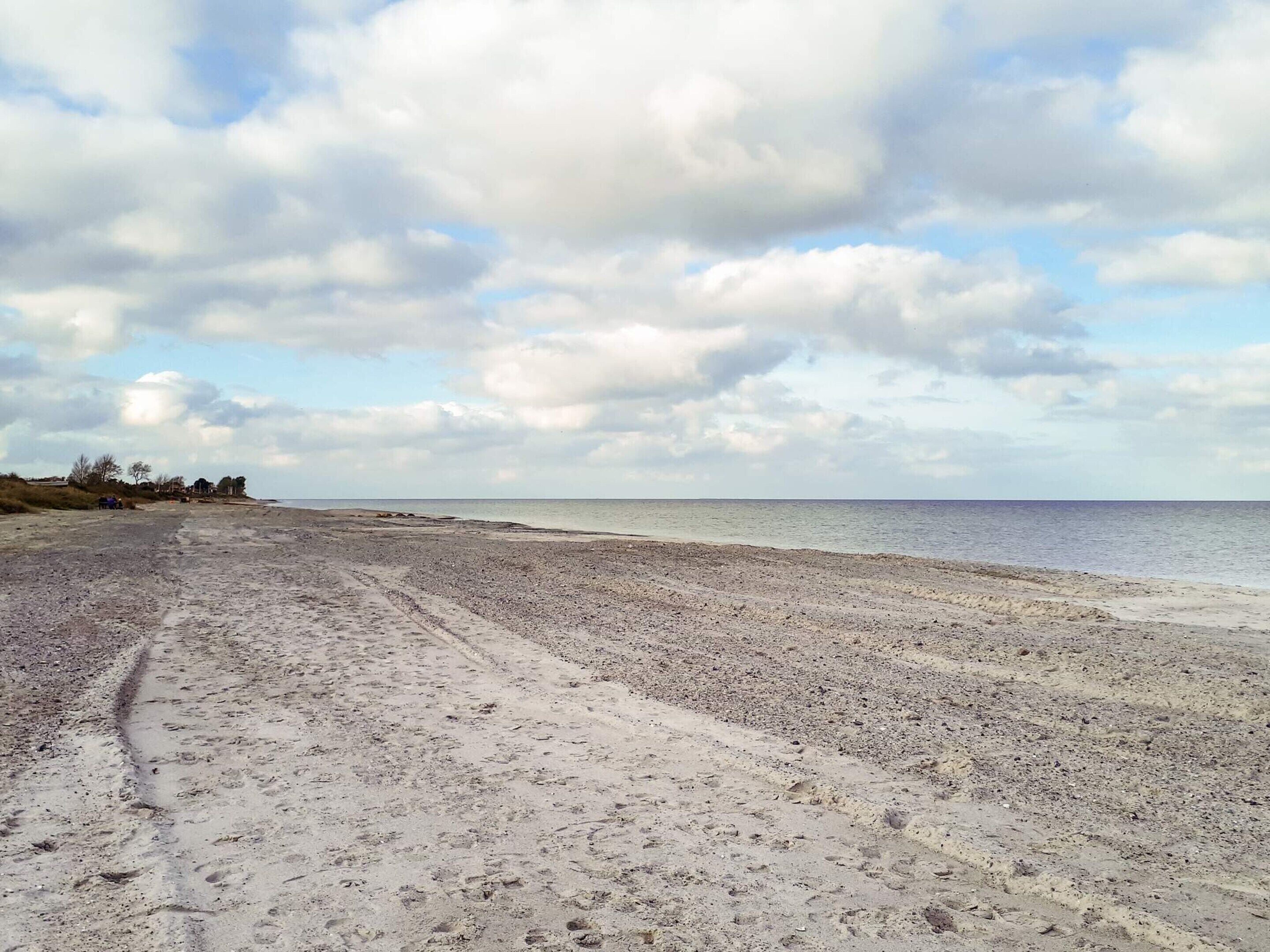 A wide sandy beach with footprints leading to the water, a clear sky, and distant trees.