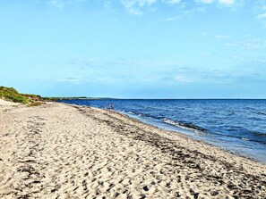 A sandy beach with gentle waves, a clear sky, and distant boats. - 2 Person Holiday Home in Otterup (Otterup)