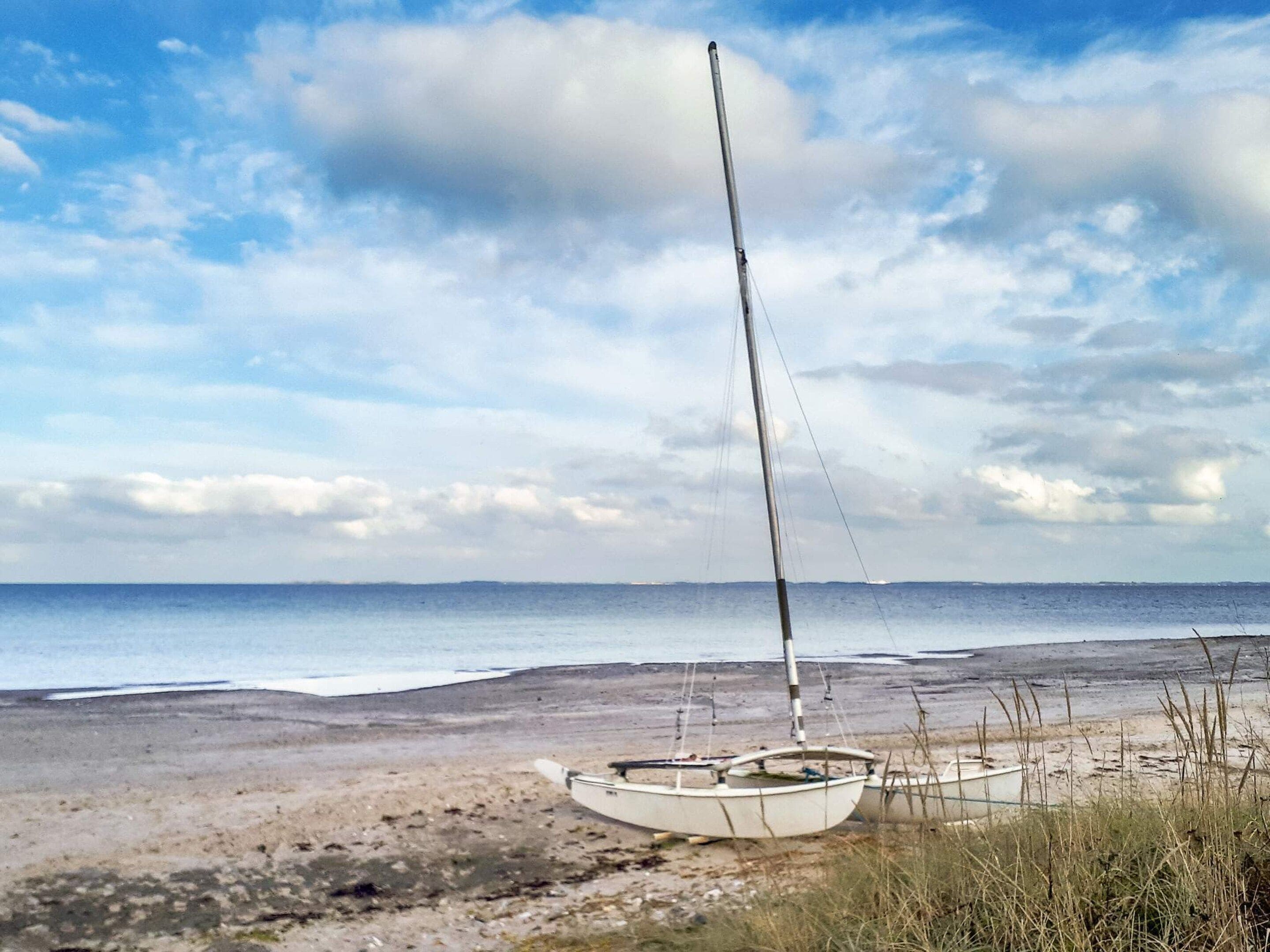 A sailboat on a sandy beach with the ocean in the background.