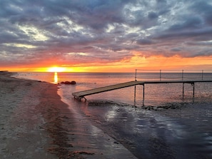 Een zonsondergang boven een strand met een houten steiger.