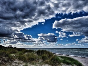 A beach with a path leading to the water, surrounded by grass and dunes.