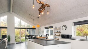 A modern kitchen with a large island, pendant lights, and a view of the outdoors. - Holiday Home in Glesborg (Glesborg)