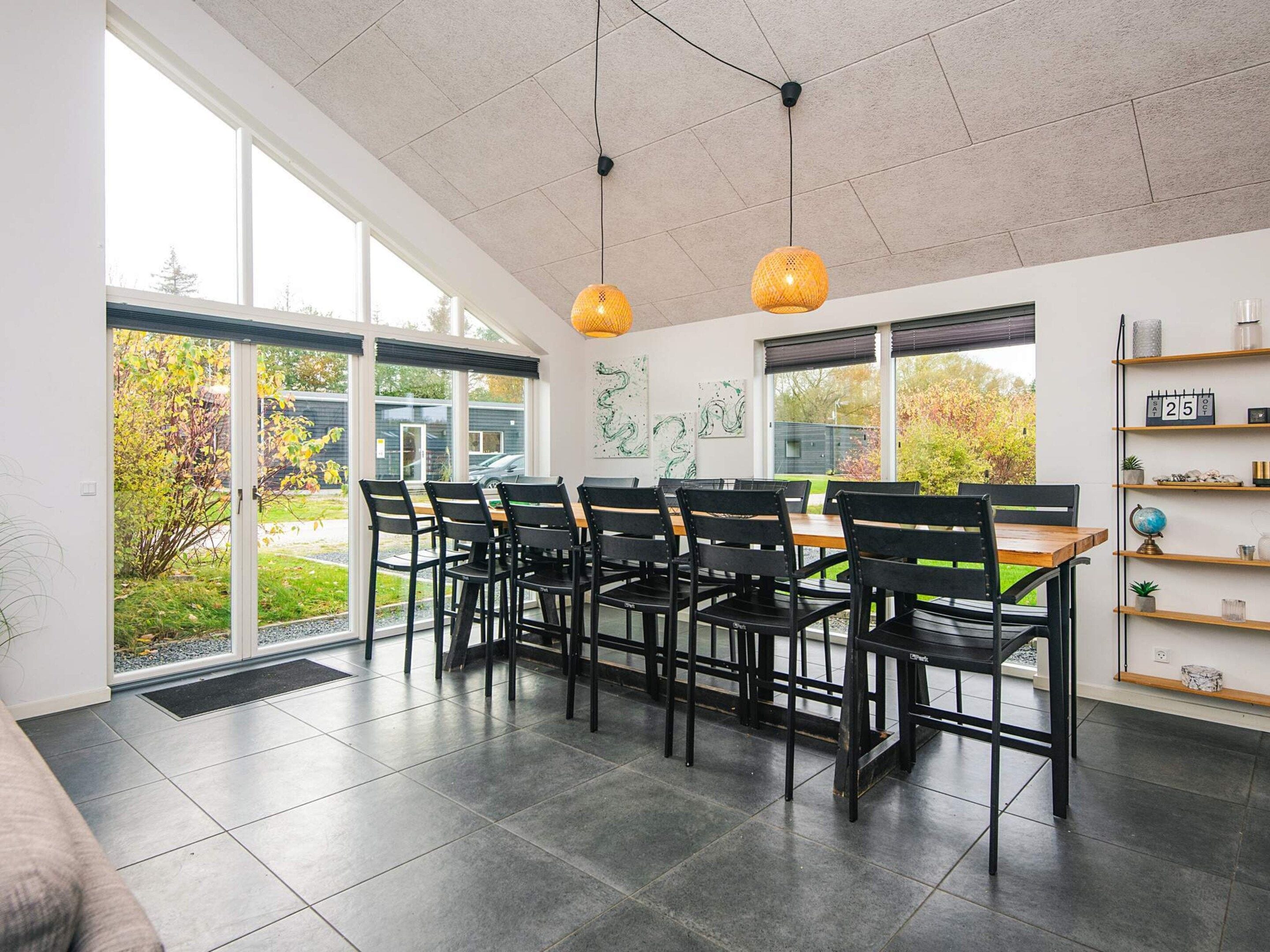 A modern dining area with a long table, black chairs, and two hanging pendant lights.