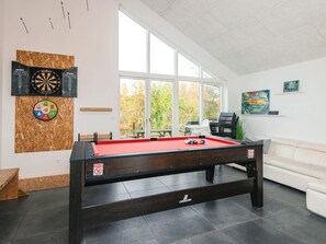 A pool table in a room with a large window, a dartboard, and a painting on the wall.