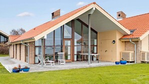 Ett modernt hus med ett sluttande tak, stora fönster och en uteplats med utemöbler.