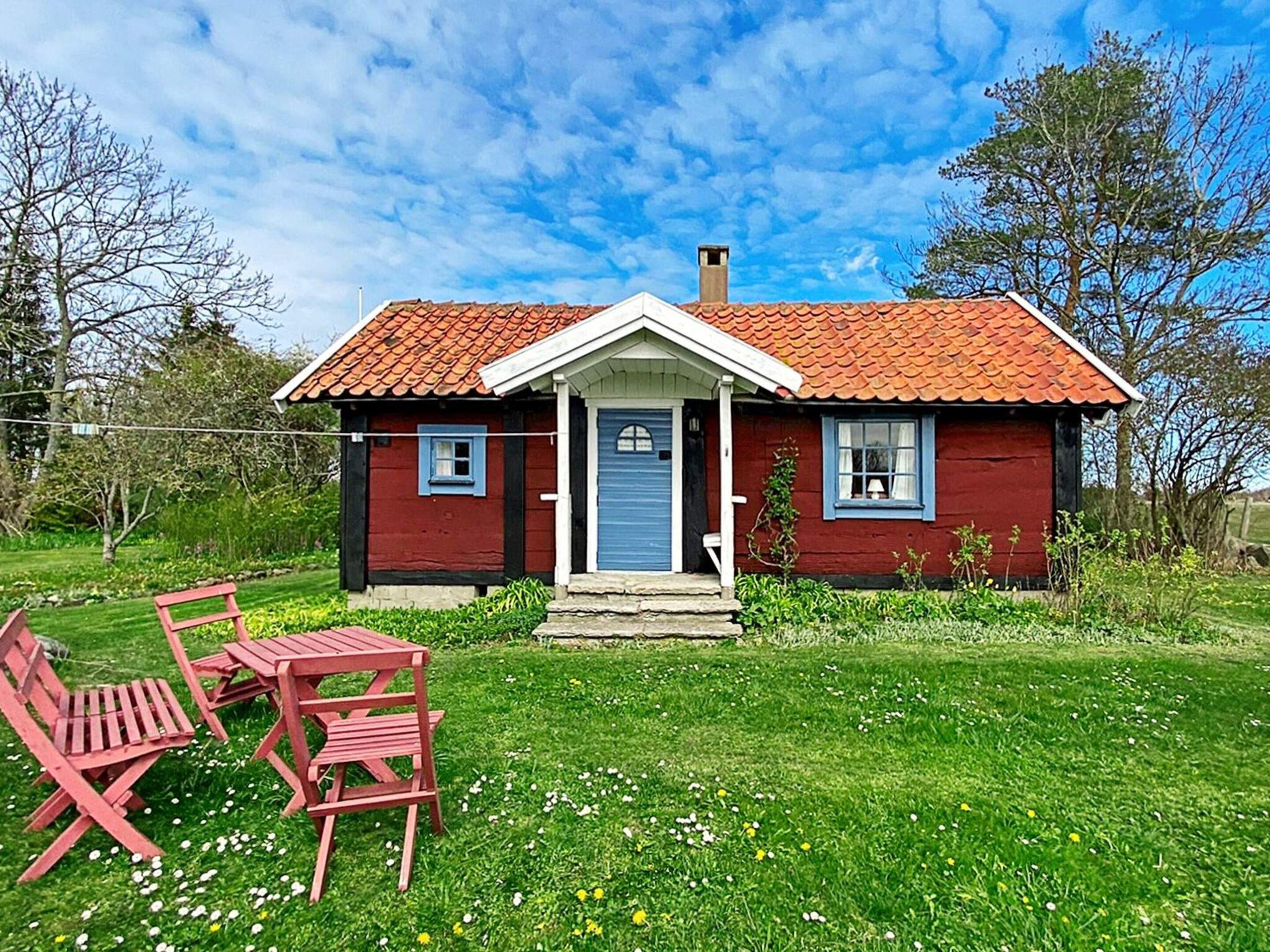 A red wooden house with a tiled roof, a front porch, and a small garden with a red table and chairs.