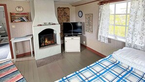 A room with a fireplace, a television, a bed, a window with curtains, and a wall clock. - 4 Person Holiday Home in Lottorp (Löttorp)