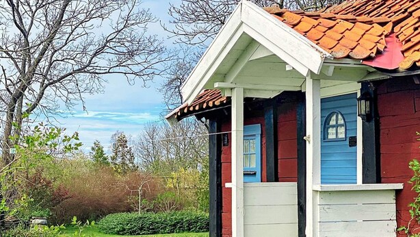 A small house with a red exterior and blue doors, surrounded by a well-maintained garden and trees. - 4 Person Holiday Home in Lottorp (Löttorp)