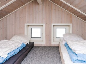 A small attic bedroom with two beds, a sloped ceiling, and two windows.