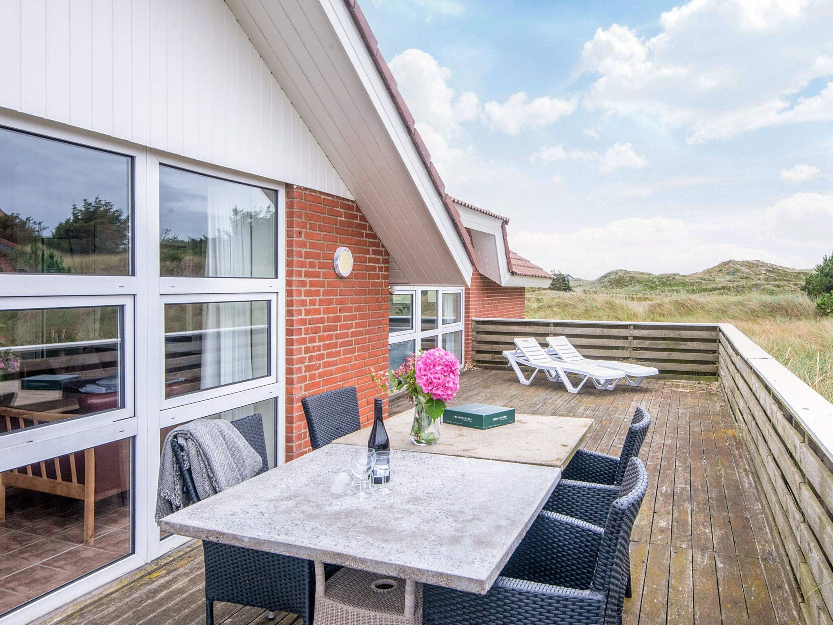 A modern outdoor patio with a table and chairs, a flower vase, and a view of the landscape.