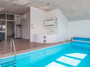 An indoor swimming pool with a clear water surface, a built-in hot tub, and a tiled floor.
