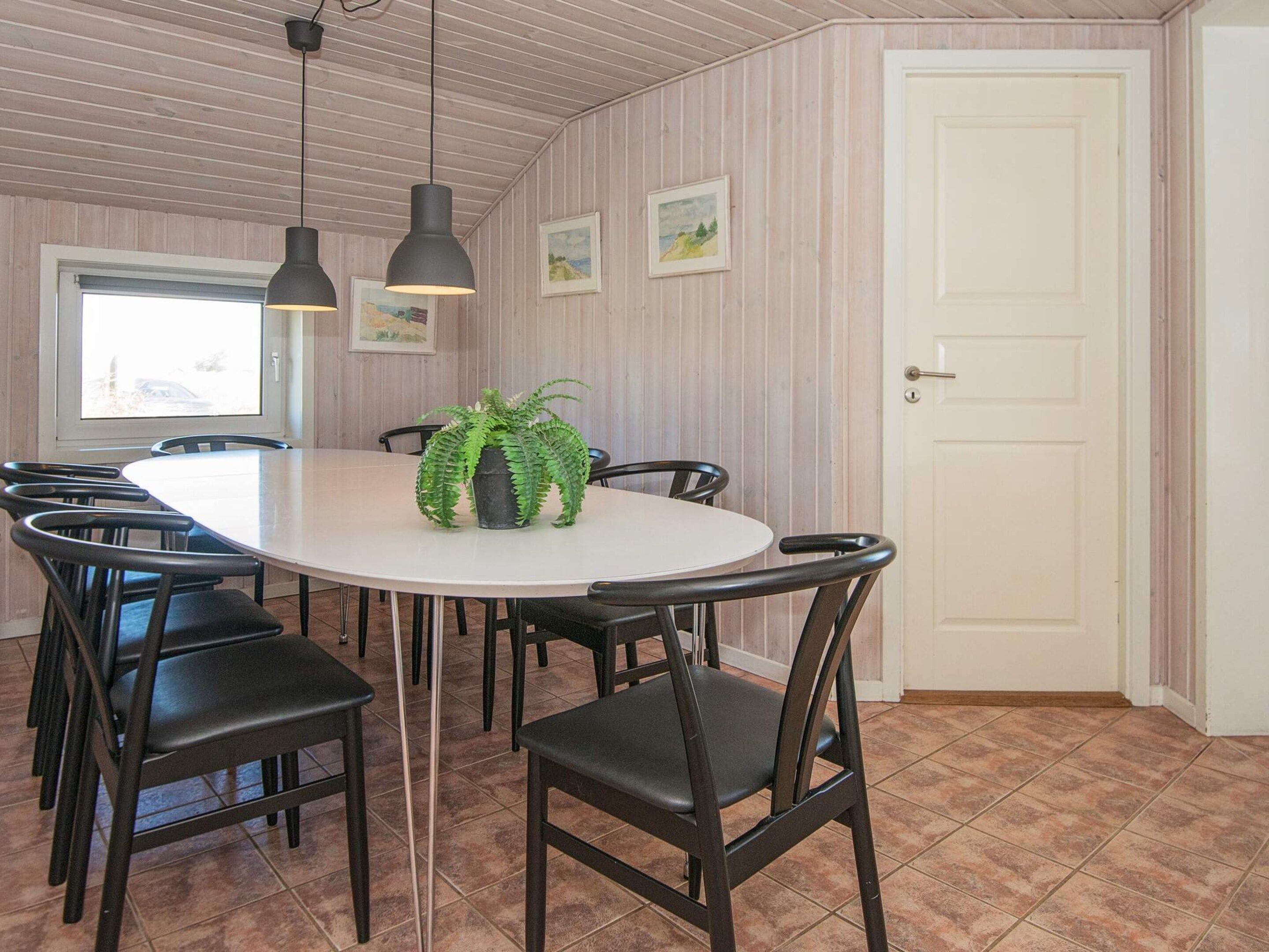 A dining area with a round table, black chairs, pendant lights, a potted plant, and a door.