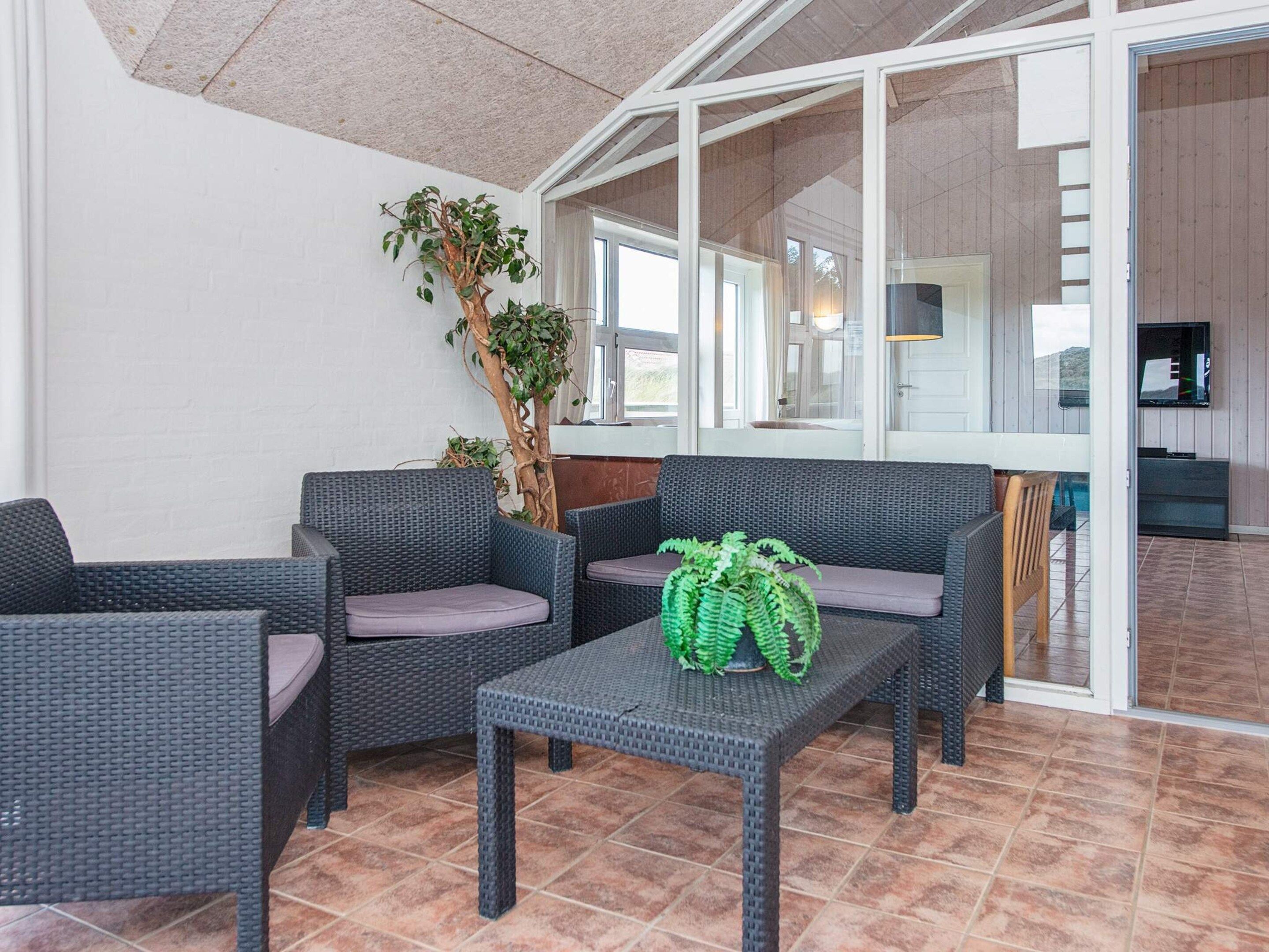 Een terras met rieten meubels, een plant in pot en uitzicht op het interieur.