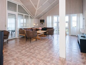 A spacious living area with a wooden ceiling, a dining table, and a sofa set.