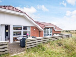 Una casa moderna con una amplia terraza, un comedor y una cocina visibles a través de grandes ventanales.