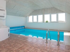 An indoor swimming pool with clear windows, a tiled floor, and a ceiling with a geometric pattern.