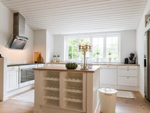 Een moderne keuken met witte kasten, een centraal eiland met wijnopslag, een ingebouwde oven en een raam met uitzicht op groen.