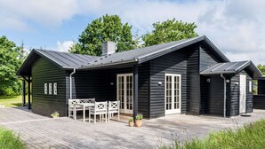 A black wooden cabin with a deck, a dining area with chairs, and a door. - 5 Star Holiday Home in Henne (Henne)
