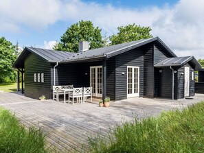 A black wooden cabin with a deck, a dining area with chairs, and a door.