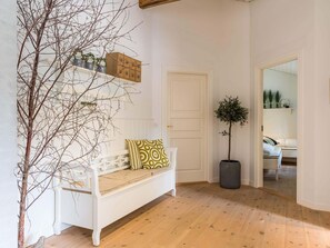 A white bench with patterned cushions, a potted tree, and a wooden floor.