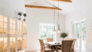 A dining area with wicker chairs, a table, hanging pendant lights, and a view through large windows. - 5 Star Holiday Home in Henne (Henne)