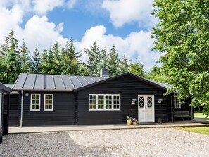 A black wooden building with a sloped roof, a front door, and windows.