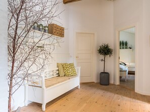 A white bench with patterned cushions, a potted plant, and a wooden floor. - 5 Star Holiday Home in Henne (Henne)