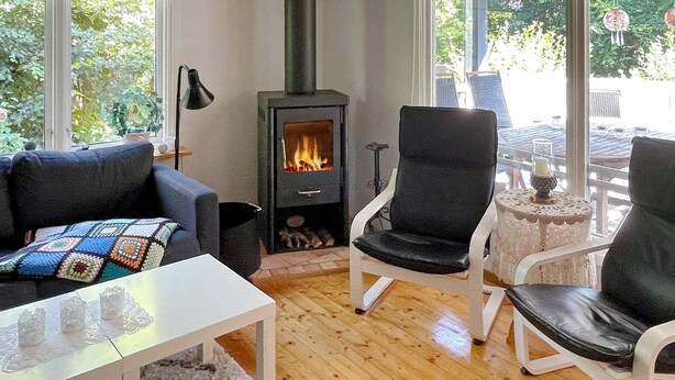 Un salon chaleureux avec un poêle à bois, une table basse blanche et deux fauteuils noirs.